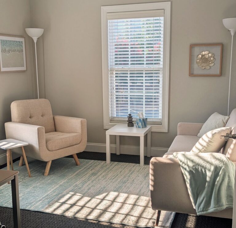 A modern, light-filled therapy room with soft neutral tones, a comfortable chair, and calming d&eacute;cor.
