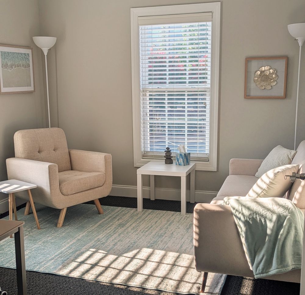 A modern, light-filled therapy room with soft neutral tones, a comfortable chair, and calming décor.