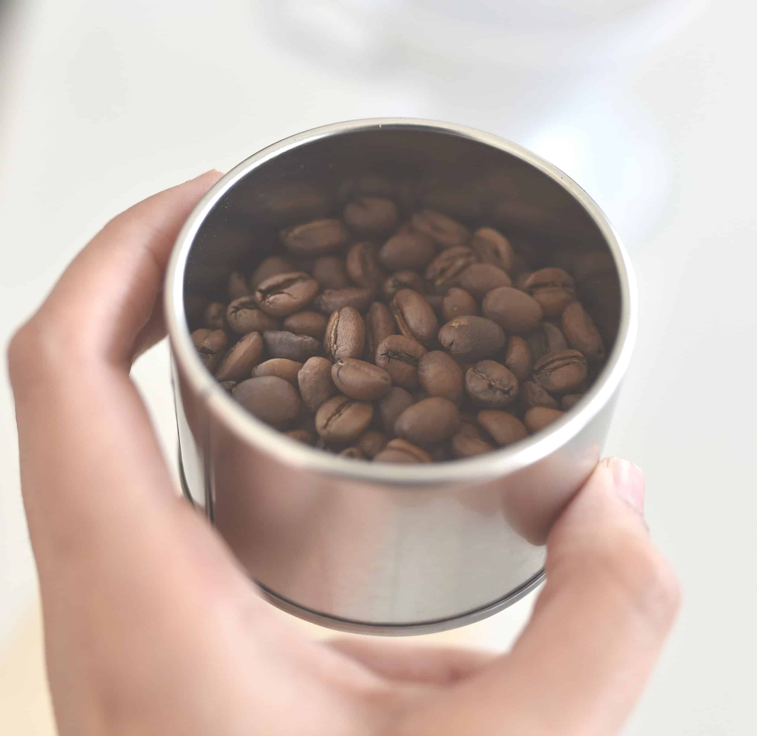 Fresh unground coffee beans in a steel cup