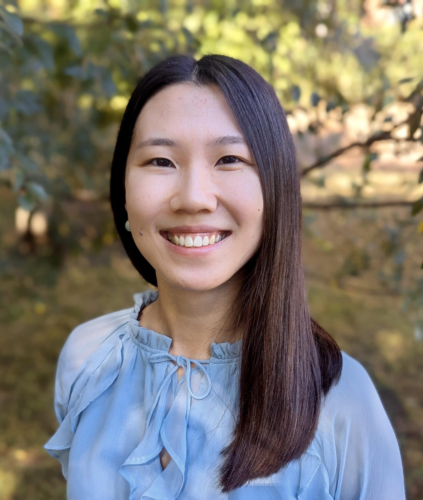 Dr. Ning Tang, PhD, trauma therapist in Raleigh, NC, smiling outdoors in soft natural light.
